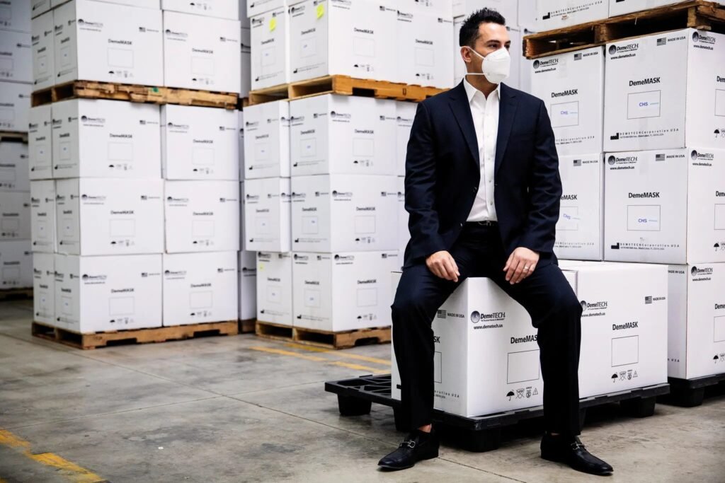 A man sitting in a mask warehouse with a mountain of inventory