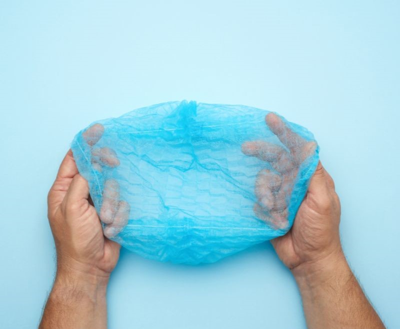 Hands holding blue surgical cap against light blue background.
