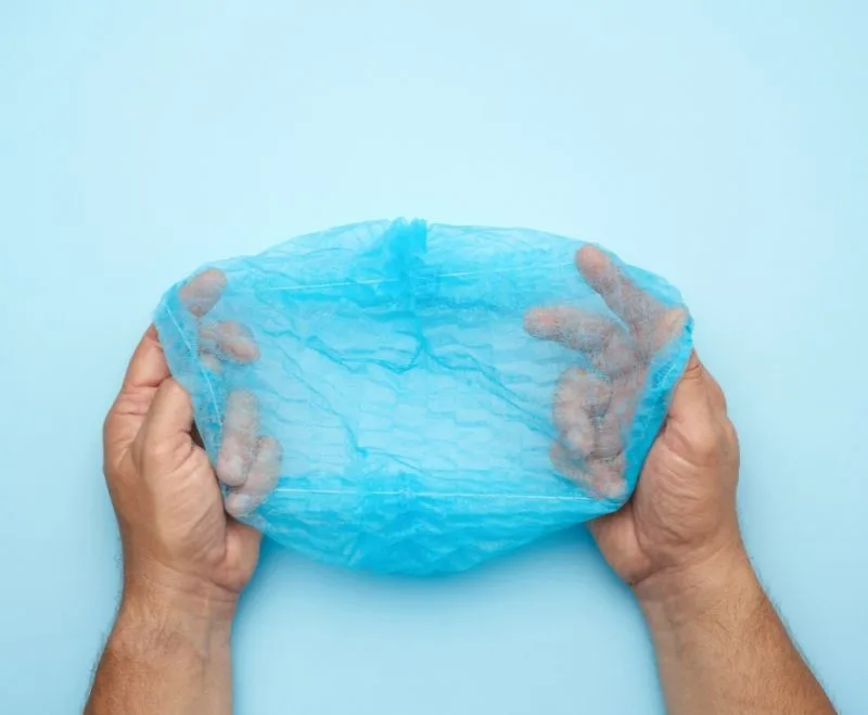 Hands holding blue surgical cap against light blue background.