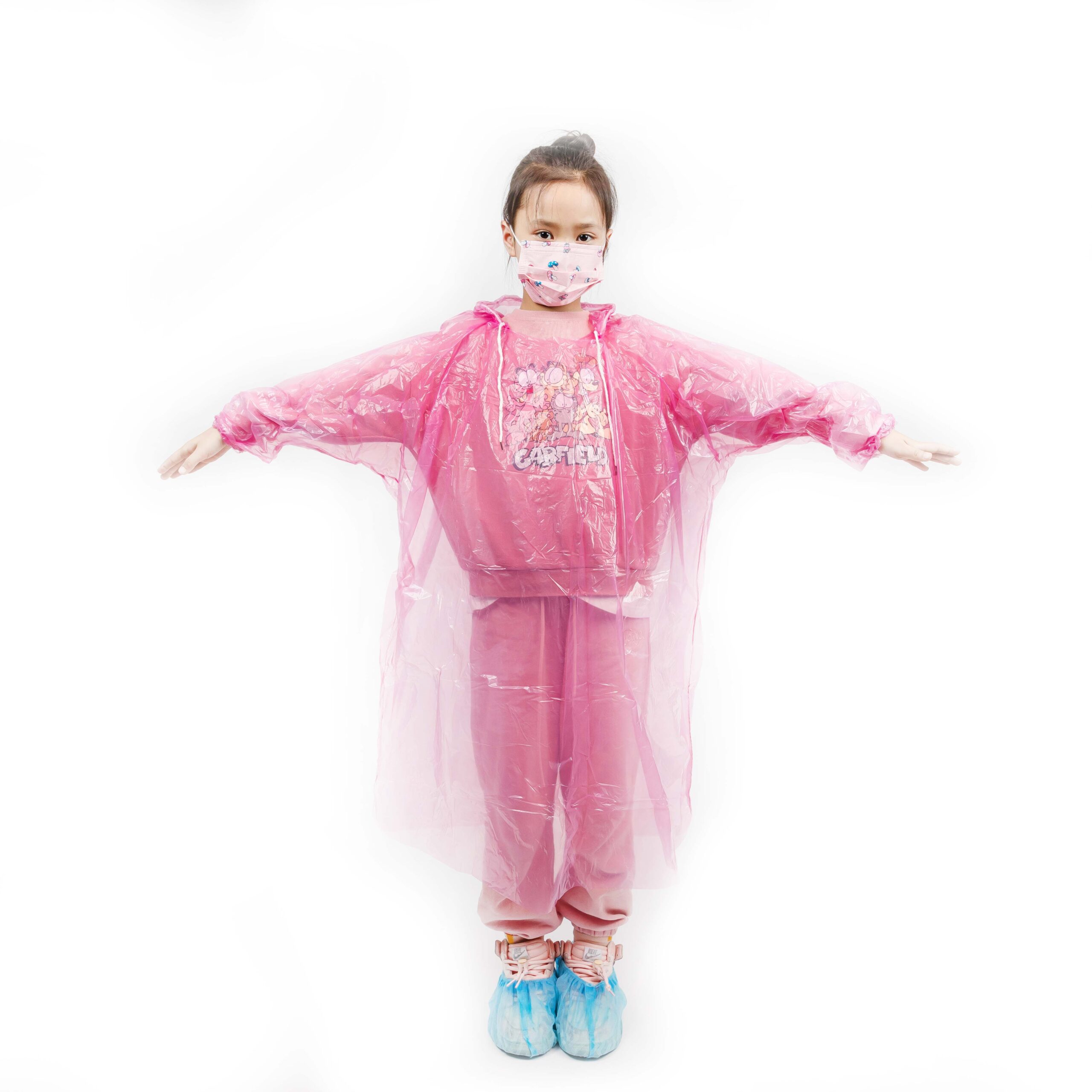 Enfant portant un imperméable et un masque roses, les bras tendus.