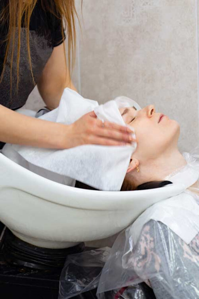 Coiffeur lavant les cheveux d'une cliente au lavabo du salon