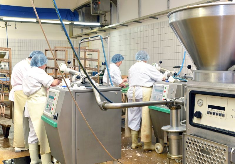 Workers operating meat processing machines in factory.